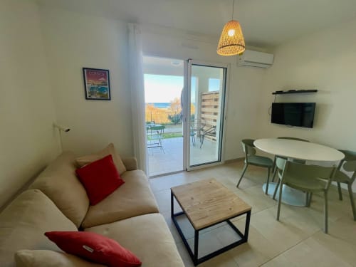 Modern apartment at Résidence Marina di Bravone in Corsica with sea view, beige sofa, dining area, and terrace access