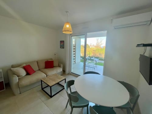 Modern apartment living area at Résidence Marina di Bravone with beige sofa, dining table, and terrace access overlooking