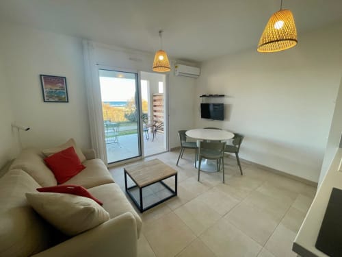 Modern apartment living room at Résidence Marina di Bravone in Corsica with sea view, wicker pendant lights, and coastal