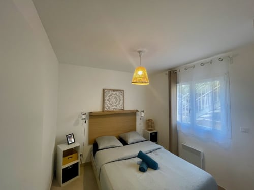 Modern bedroom at Résidence Marina di Bravone with wooden headboard, yellow pendant light, and terrace doors overlooking