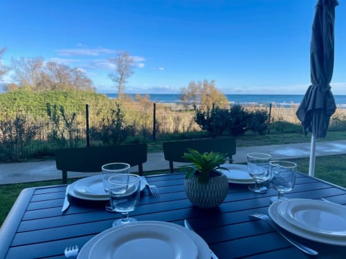 Beachfront dining setup at Résidence Marina di Bravone, Linguizzetta with ocean view, place settings, and umbrella