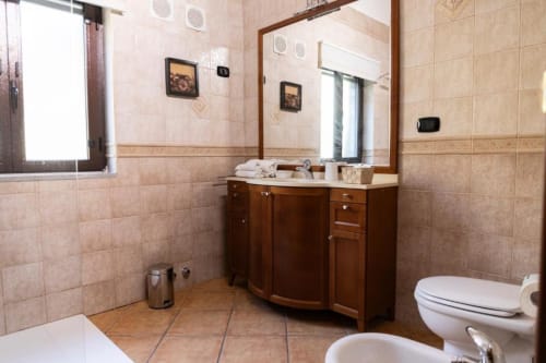 Elegant bathroom in Mas Collection's San Bartolomeo room, Bari, with wooden vanity, mirror, bidet, toilet, and tiled floors.