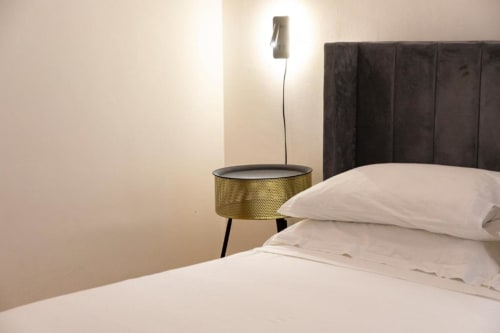 Modern bedroom at Mas Collection hotel in Bari with white bedding, dark upholstered headboard, and brass side table with