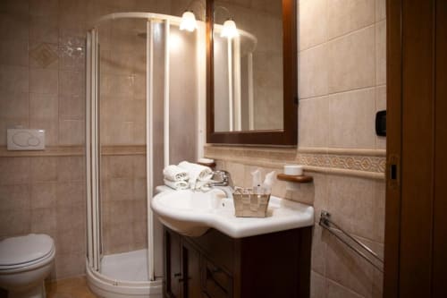 Elegante bagno nella Mas Collection Deluxe Room di Bari con box doccia in vetro, lavabo bianco, mobile scuro e dettagli beige