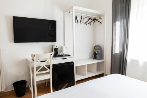 Camera moderna con TV a parete, scrivania bianca, sedia, armadio con attaccapanni e letto presso Mas Collection a Bari