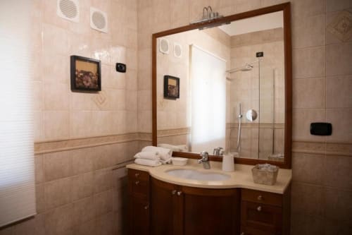 Modern bathroom at Mas Collection Bari with large mirror, wood vanity, white towels, and beige tile walls