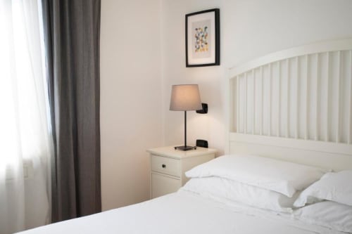 Camera da letto moderna nella Mas Collection Bari con letto bianco, vista giardino, lampada comodino e arredamento neutro