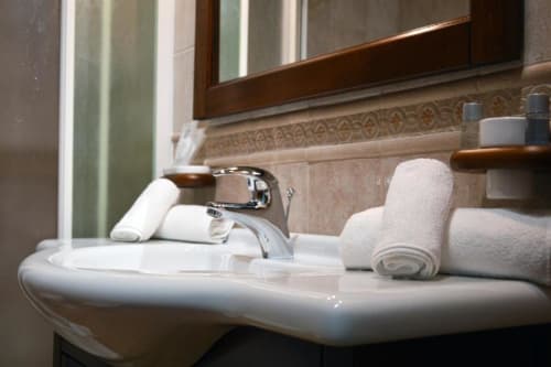 Lavabo moderno con rubinetto cromato, asciugamani arrotolati e specchio nella Deluxe Room di Mas Collection a Bari