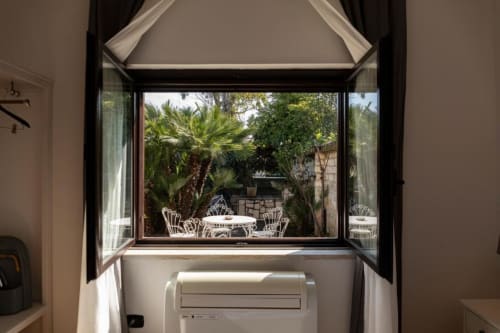 Finestre francesi aperte su un rigoglioso giardino interno con palme e arredi da patio bianchi di Mas Collection Bari