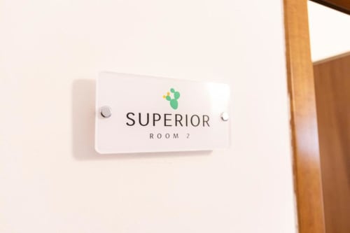 White room sign reading 'SUPERIOR ROOM 2' with leaf logo for Mas Collection hotel in Bari
