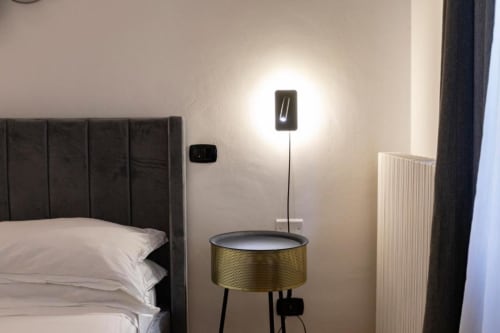 Modern bedroom in Mas Collection Bari with black upholstered bed, brass accent table, pendant lighting, and contemporary wall