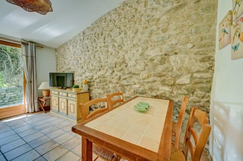 Salle à manger de maison en pierre avec table et chaises en bois, vue sur jardin, Domaine Bellavigne Gîtes, Forcalquier