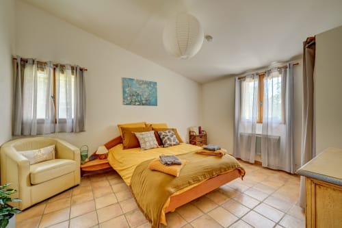 Chambre lumineuse au Gîte Agave de Domaine Bellavigne à Forcalquier, avec literie jaune, fauteuil crème et vue sur le jardin