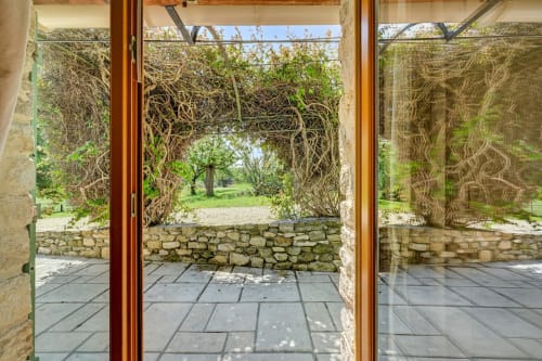 Terrasse en pierre avec portes vitrées donnant sur le jardin luxuriant du gîte Domaine Bellavigne à Forcalquier, France