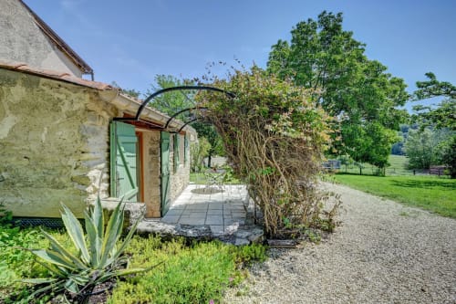 Entrée de cottage en pierre au Domaine Bellavigne avec portes vertes, tonnelle courbe et jardin luxuriant à Forcalquier