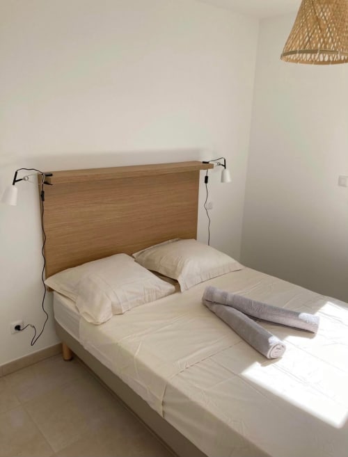 Camera da letto nella residenza Marina di Bravone con testata in legno, biancheria bianca e asciugamani arrotolati