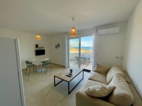 Moderna sala living con vista mare presso Résidence Marina di Bravone, divano beige, zona pranzo e accesso terrazza