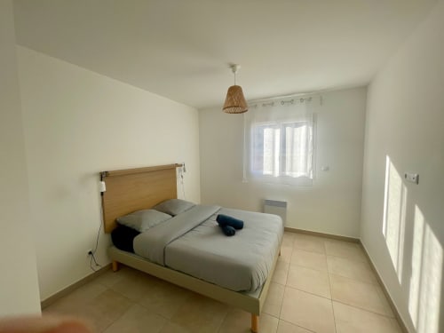 Chambre lumineuse à la Résidence Marina di Bravone à Linguizzetta avec lit en bois, luminaire suspendu tressé et accès à la terrasse