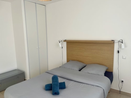 Chambre moderne à la Résidence Marina di Bravone avec tête de lit en bois, literie grise et deux serviettes bleues sur le lit