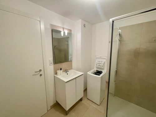 Salle de bain moderne d'un T3 à la Résidence Marina di Bravone avec vasque, machine à laver et douche vitrée
