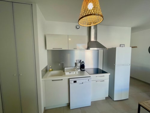 Cuisine moderne de l'appartement T3 Marina di Bravone avec armoires blanches, électroménagers inox et luminaire suspendu tressé