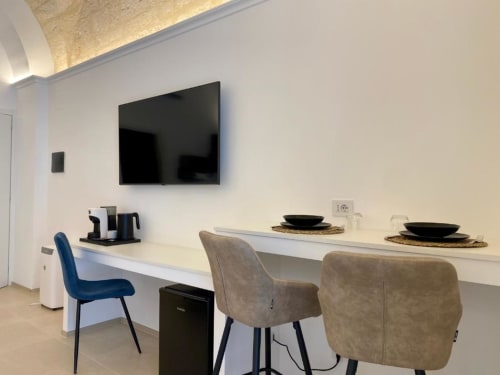 Zona pranzo moderna con televisione, scrivania bianca, sedie beige e tavolo apparecchiato nella Mas Collection di Bari