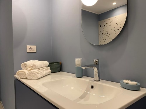 Bagno moderno nell'appartamento Mas Collection Bari con lavabo bianco, rubinetto cromato, asciugamani arrotolati e specchio in terrazzo