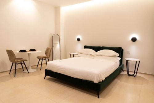 Camera moderna della Mas Collection Bari con letto imbottito nero, biancheria bianca, arredamento minimalista e illuminazione contemporanea