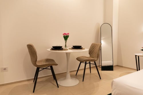 Elegante zona pranzo nell'appartamento Mas Collection a Bari con tavolo rotondo, sedie beige, fiori rosa e specchio ad arco