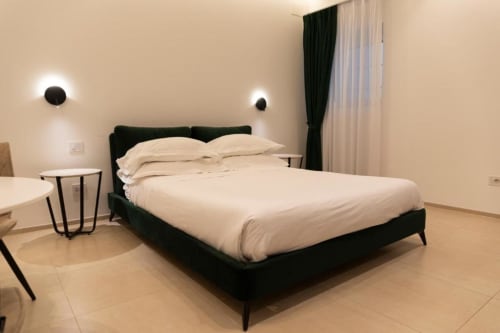 Camera da letto moderna con letto nero, biancheria color crema e illuminazione a parete nell'appartamento Mas Collection a Bari