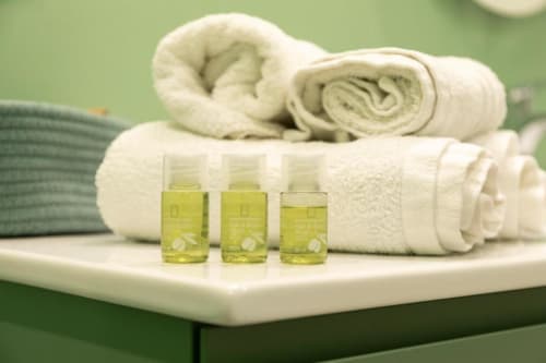 Tre piccole bottiglie di prodotti da bagno omaggio con asciugamani bianchi arrotolati presso l'appartamento Mas Collection a Bari