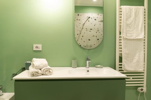Bagno moderno con pareti verdi, lavabo bianco, specchio rotondo e portasciugamani nell'appartamento Mas Collection a Bari