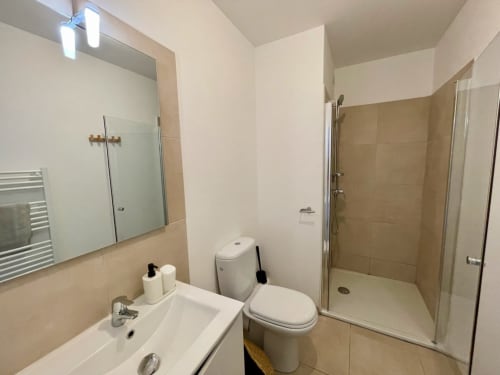 Modern bathroom at Résidence Marina di Bravone with toilet, sink, mirror, shower enclosure and beige tile accents