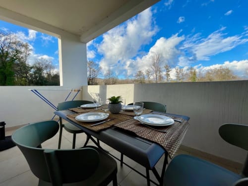 Modern terrace dining area at Résidence Marina di Bravone with set table, green chairs, and scenic sky views in Linguizzetta