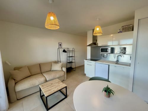 Modern studio apartment at Résidence Marina di Bravone with kitchenette, beige sofa, dining area and pendant lighting