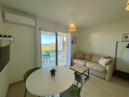 Modern T2 apartment at Marina di Bravone with sea view, beige sofa, dining table, and terrace overlooking beach in