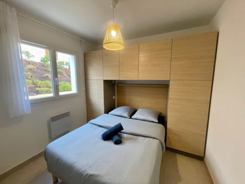 Modern bedroom at Résidence Marina di Bravone with light wood built-in wardrobes, double bed, and window overlooking garden
