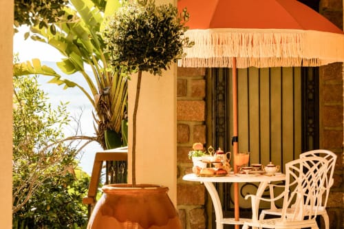 Terrazza soleggiata dell'Hôtel Villa Martini ad Ajaccio con sedie bianche, tavolo da pranzo, ombrellone arancione e piante mediterranee