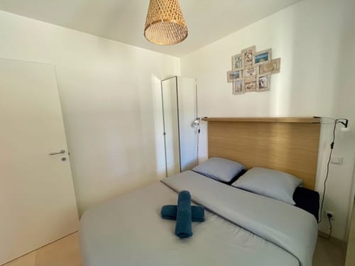 Accogliente camera da letto presso la Résidence Marina di Bravone a Linguizzetta con letto in legno, biancheria bianca e lampada a soffitto intrecciata