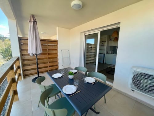 Balcone dell'appartamento fronte mare della Résidence Marina di Bravone con tavolo da pranzo, sedie verdi e vista sul mare a Linguizzetta