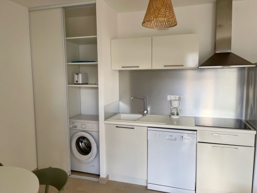 Cucina moderna e compatta con mobili bianchi, elettrodomestici in acciaio inox e lavatrice integrata in ripostiglio