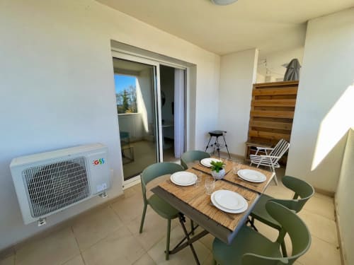 Modern dining area at Marina di Bravone with set table, green chairs, sea view balcony, and air conditioning unit