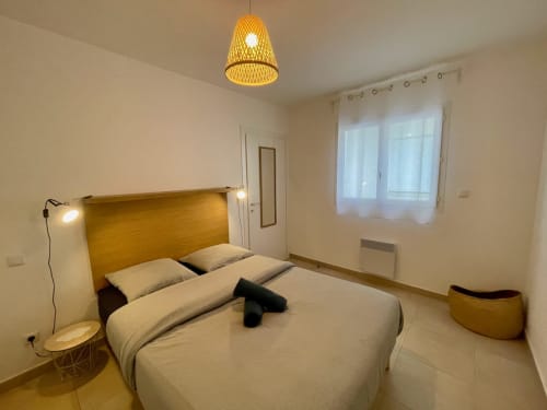 Modern bedroom at Résidence Marina di Bravone with wooden headboard, pendant light, and sea view window