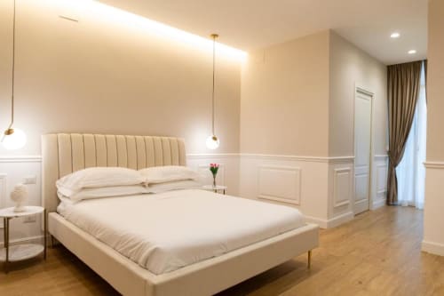 Camera da letto beige nella collezione Mas di Bari con letto crema, luci a sospensione e pavimento in legno