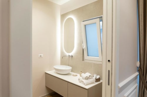 Bagno moderno nell'appartamento Mas Collection Bari con specchio ovale illuminato, lavabo bianco e finestra con vista