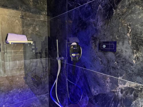 Bagno moderno con pareti in marmo scuro e illuminazione blu presso Mas Collection Bari, dotato di doccia a cascata e cromature