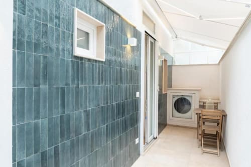 Moderna lavanderia con piastrelle blu, lavatrice e sedie in legno nell'appartamento Mas Collection a Bari