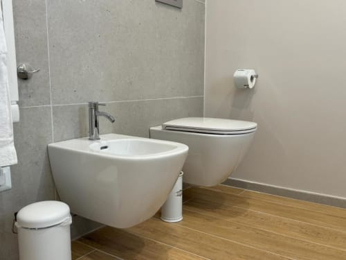 Bagno moderno con bidet e wc sospesi, lavabo in ceramica e pavimento in legno presso l'hotel Mas Collection di Bari