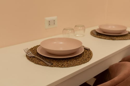 Tavolo elegantemente preparato nella Pink Room di Mas Collection a Bari con stoviglie rosa, tovagliette tessute e posizionamento delle forchette.