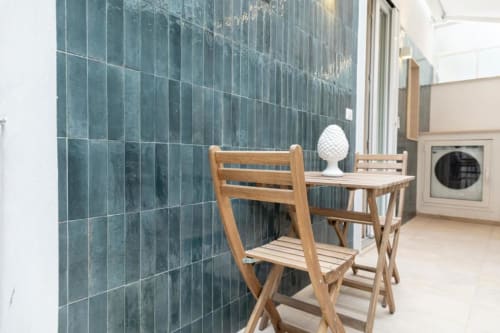 Sedia e tavolo in legno nell'appartamento Mas Collection con parete in piastrelle turchesi e vista sul cortile, Bari
